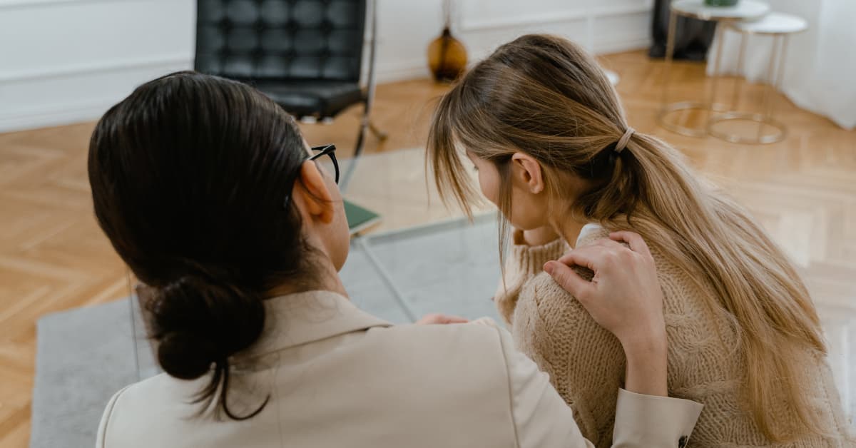 A woman comforts another women, as seen from behind.