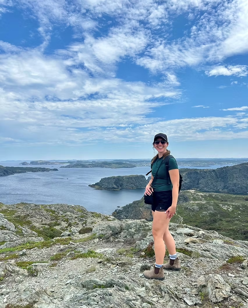 Michaela at a rocky lookout, smiling at the camera with water and islands in the background.