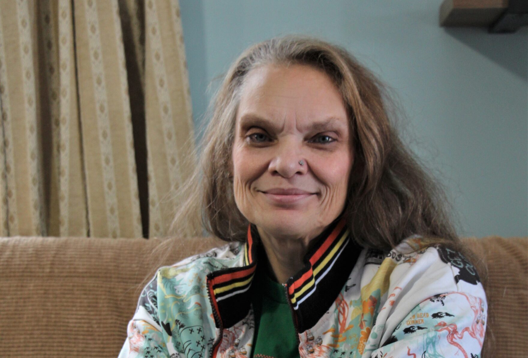 Joanne sits on a couch in her home smiling.