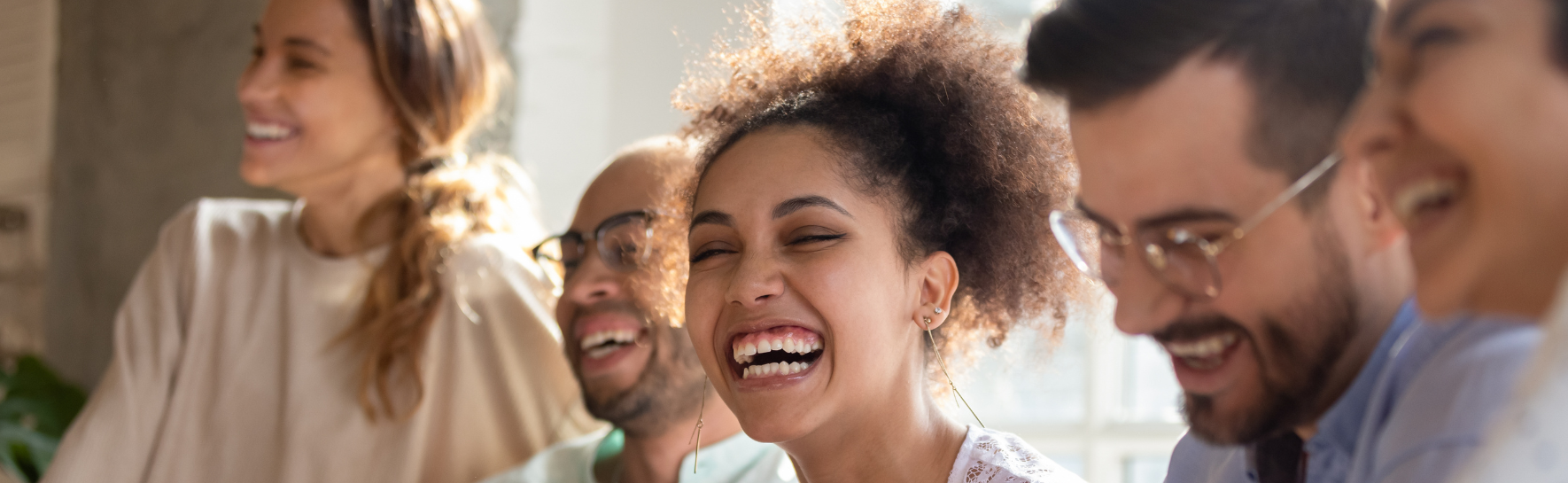 A group of young adults smiling and laughing with the sun behind them.